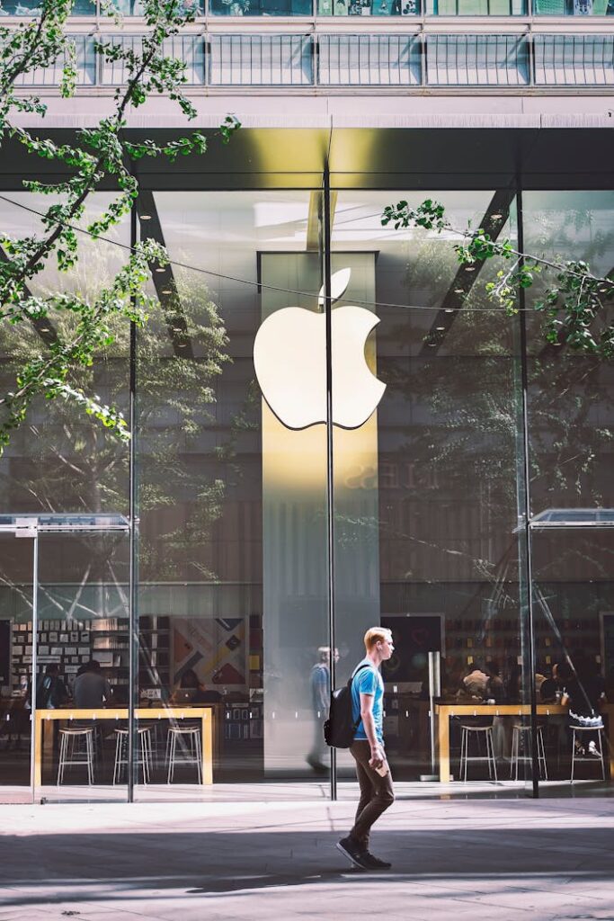 A casual scene of a man walking past the iconic glass facade of an Apple Store in Beijing, China.